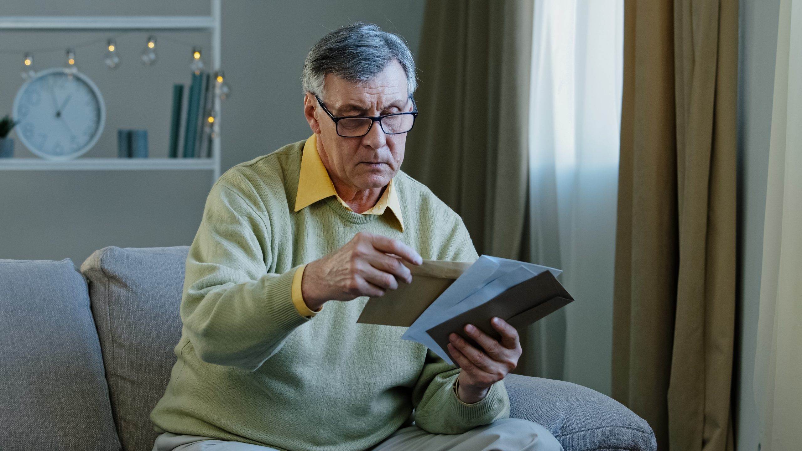 Older man with glasses sorting letters in living room.